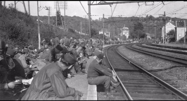 Upon arriving at the cost of northern France, all soldiers were sent to one of the camps and transferred from one to another until they were about to be sent on the battlefield. Image showing hundreds of them waiting for a train on a railroad not knowing what their next or last stop will be. Photo Credit: Rescued Film Project