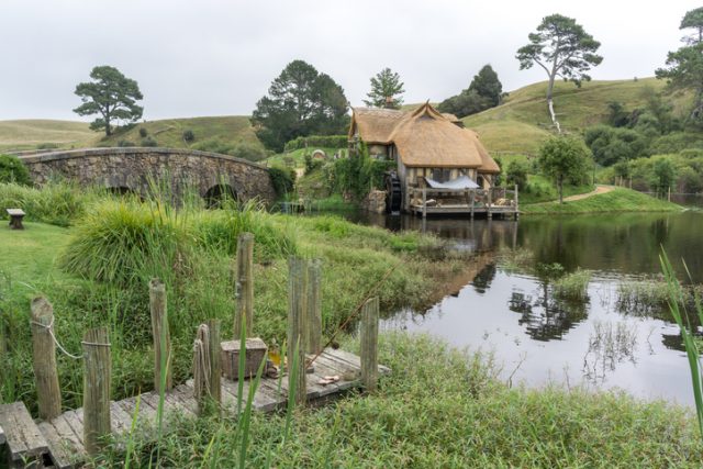 hobbiton mill and double arched bridge with lake reflection in hobbiton movie set, new zealand.