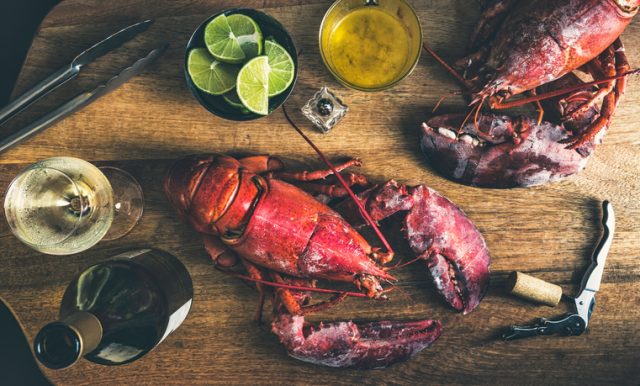 Directly above view of a wood table with two red and fresh lobsters ready to eat, accompanied by white wine lemon and butter. The picture is an studio shot with a combination of natural and artificial light to achieve a very intimate ambiance.