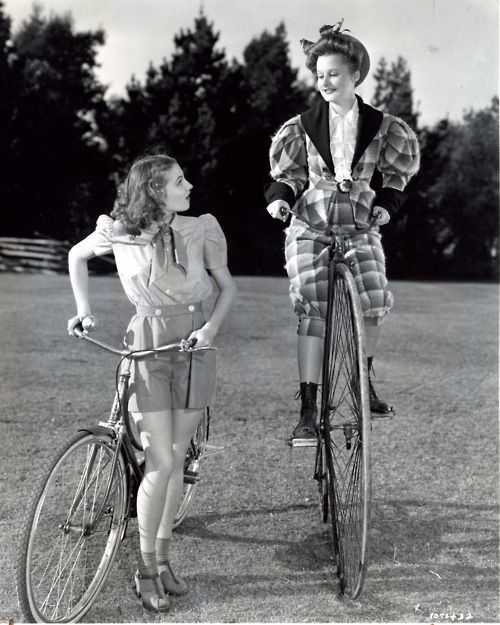 Lynne Carver riding a penny farthing bike while Jo Ann Sayers walking with a bike