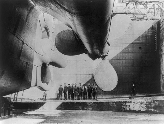 Shipbuilders gather underneath one of the Titanic's propellers, 1912. source