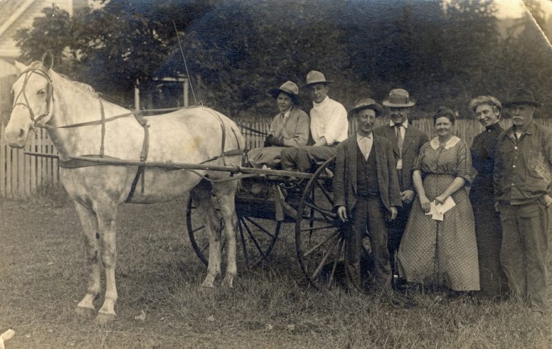 An unidentified Rural Free Delivery carrier posed in his two-wheeled mail cart with patrons from along his new mail route. Location is not identified in the image. 1905