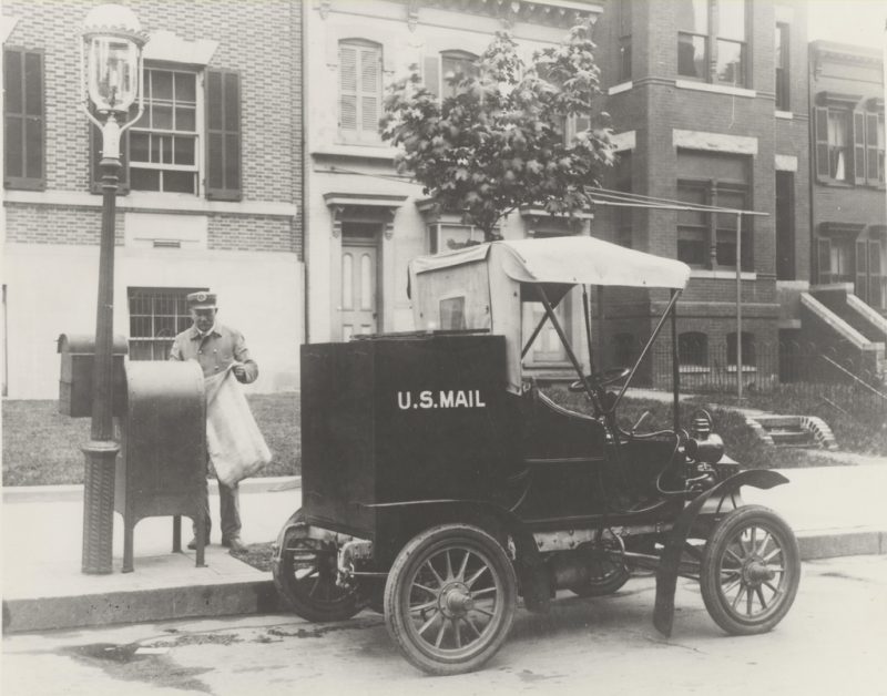 Letter carrier removes mail from a sidewalk collection box. 1906