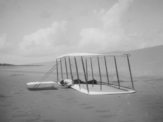 Wilbur just after landing the 1901 glider. Glider skid marks are visible behind it, and marks from a previous landing are seen in front; Kill Devil Hills, North Carolina.