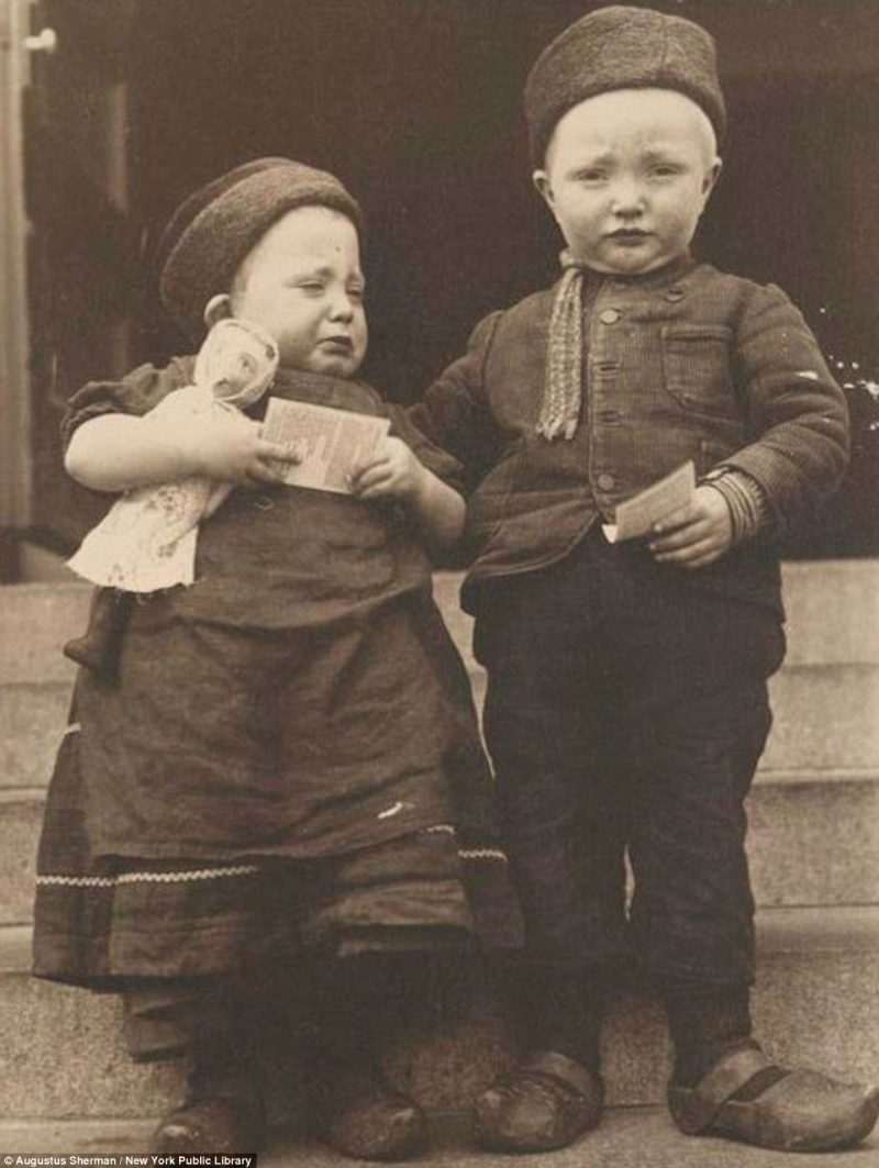 A couple of Dutch children, dressed in their traditional clogs and costume, clutch onto their immigration forms in the pictures by photographer Augustus Sherman 