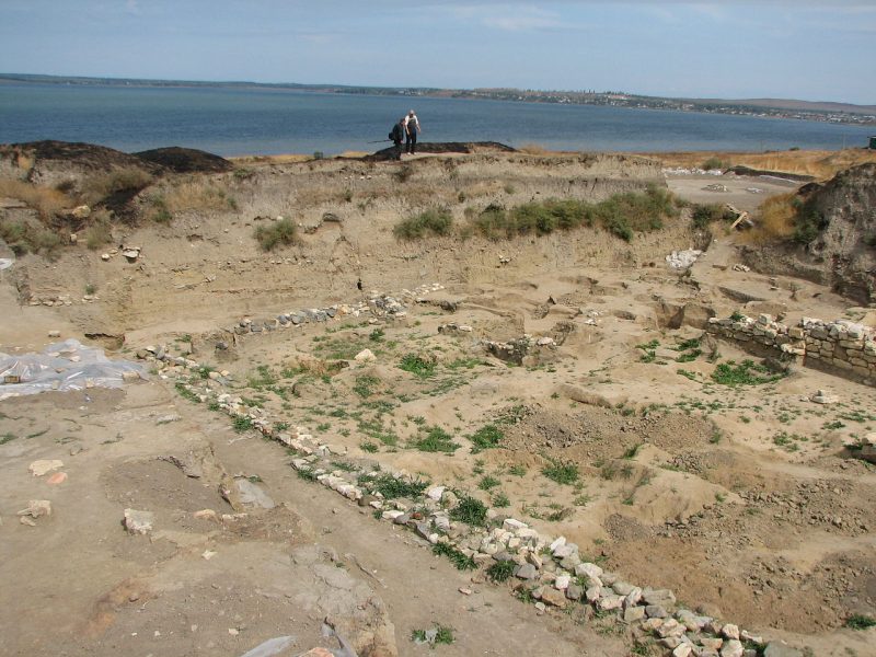 he remains of the wall of a small structure are seen in the foreground, the Sea of Azov is visible in the background.