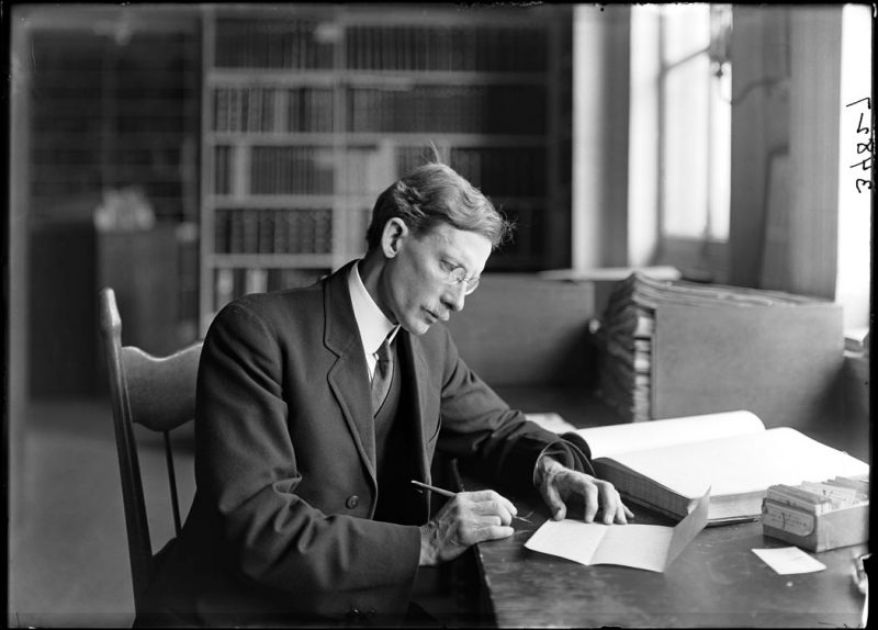 Dr. Jesse M. Greenman, Assistant Botany Curator in the Herbarium sitting at his office desk, using a pen to make entries into the catalogue book, 1912