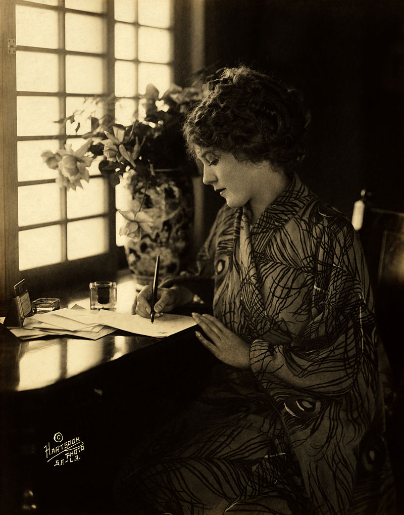 Mary Pickford, wearing a kimono, writing at a desk .Source