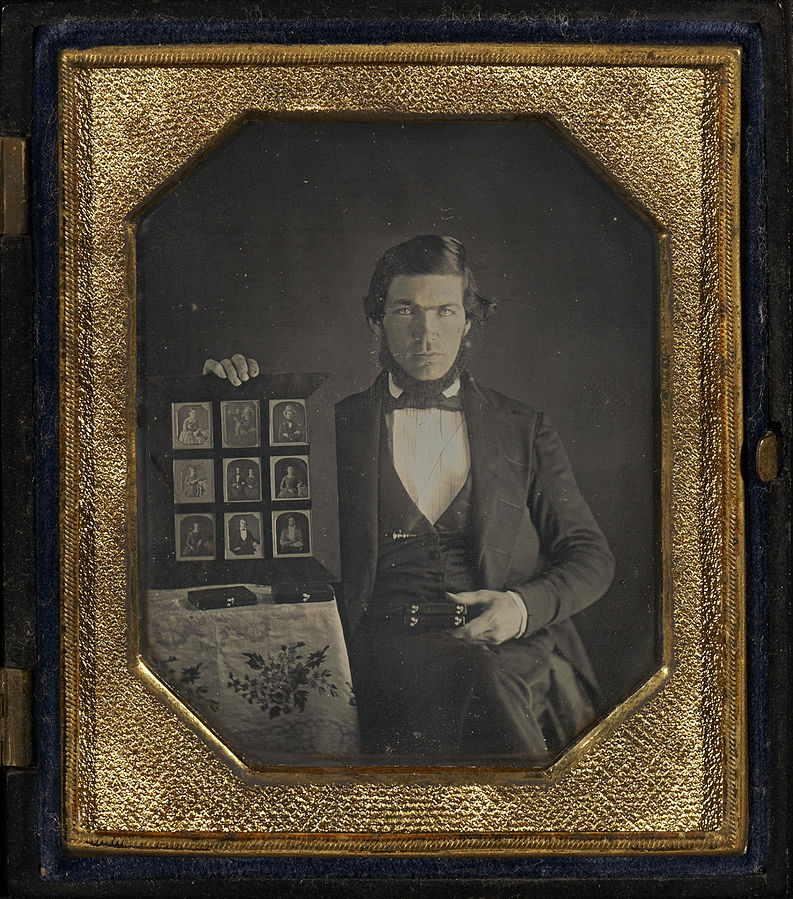 Portrait of a Daguerreotypist Displaying Daguerreotypes and Cases. source