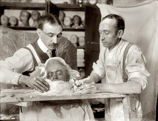 Two men in the process of making a death mask