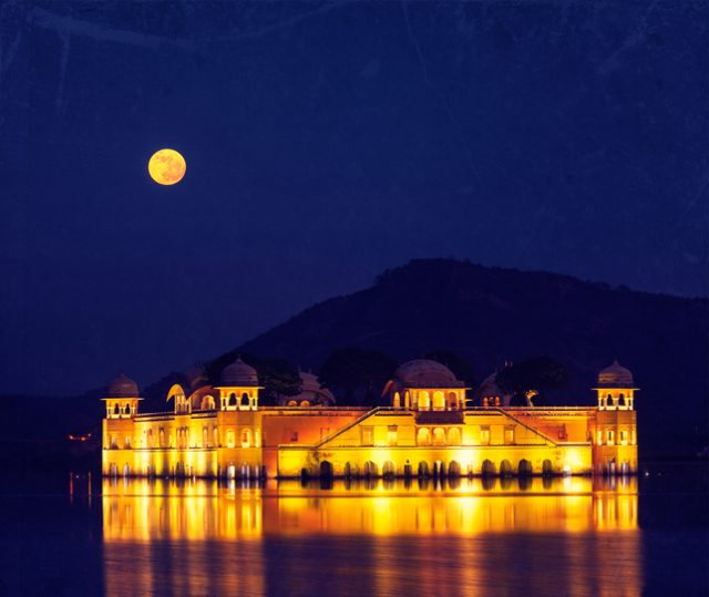 Vintage retro hipster style travel image of Rajasthan landmark – Jal Mahal (Water Palace) on Man Sagar Lake at night in twilight with grunge texture overlaid. Jaipur, Rajasthan