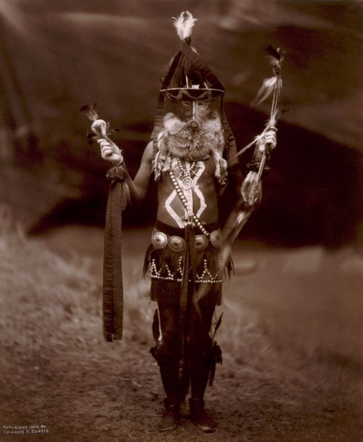 A Navajo man, full-length, in ceremonial dress including mask and body paint.