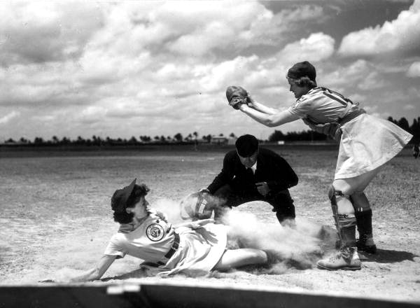All-American Girls Professional Baseball League player Marg Callaghan sliding into home plate as umpire Norris Ward watches, Opa-locka, Florida.