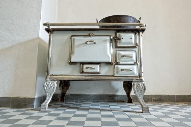 Front view of an old white-colored oven. It fits well with the bare white walls and the choice of tiles for the floor.
