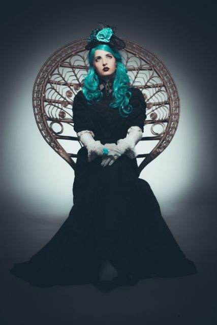 Dramatic full length portrait of Goth-style woman sitting in a peacock chair