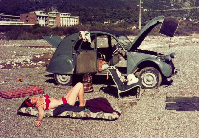 Original vintage colour slide from 1960s, young woman relaxing on a beach with her car.