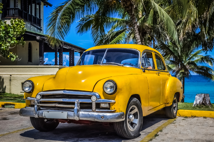 American beautiful yellow classic parked under palms in Varadero Cuba