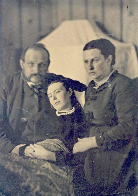 Victorian era post-mortem family portrait of parents with their deceased daughter.