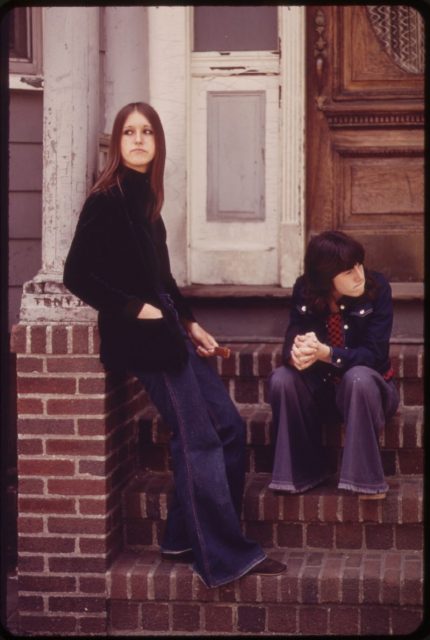 Virginia Shea and Sharon Cardillo on the doorstep of a house on Neptune Road, Boston, Massachusetts, 1973. Virginia has chosen a suede-look jacket and turtleneck to complement her flared pants, while Sharon shows us how double denim works.