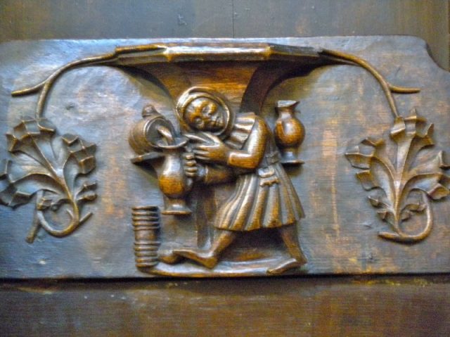 A misericord showing ale being drawn from a cask by alewife in St Laurence, Ludlow, Shropshire, England. Photo by Charlesdrakew CC BY SA 3.0