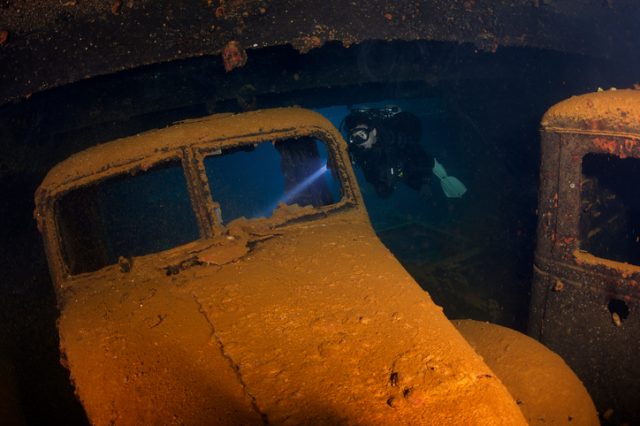Female diver explores a car from the 1940s in one of the holds on the wreck of the Hoki Maru, Truk Lagoon. The shipwreck is a very popular dive for experienced divers.