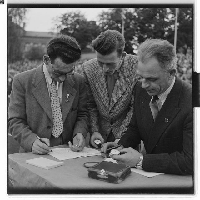 Men synchronizing their pocket watches. Photo by Arne F. Køpke – National Archives of Norway CC BY-SA 4.0