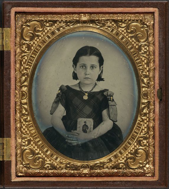 Girl in a mourning dress holding a framed photograph of her father, who presumably died during the American Civil War.