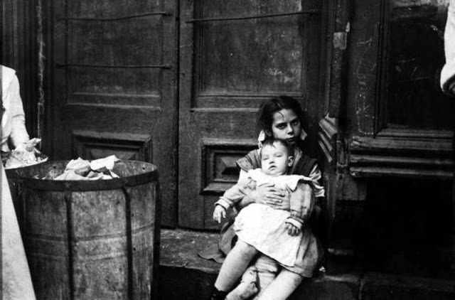 Girl sitting on doorstep with baby on her lap, New York, circa 1890.