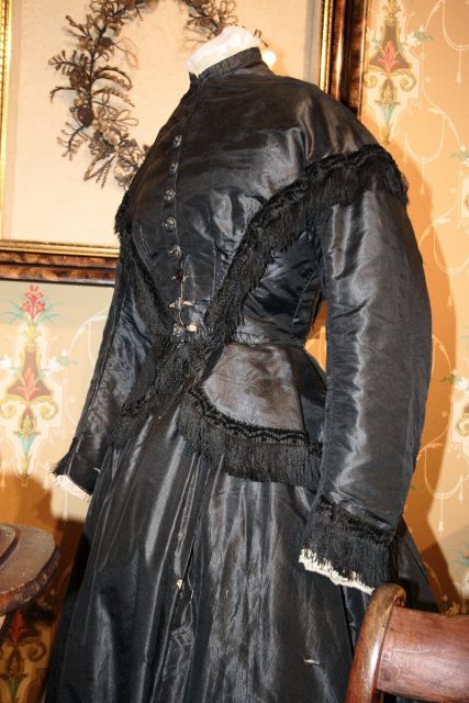 Woman’s mourning dress (1867-1869): silk bodice and skirt with black fringe, white lace cuffs, and white guaze collar. Museum of Funeral Customs, Springfield, Illinois, 2006. Photo by Robert Lawton CC BY-SA 2.0