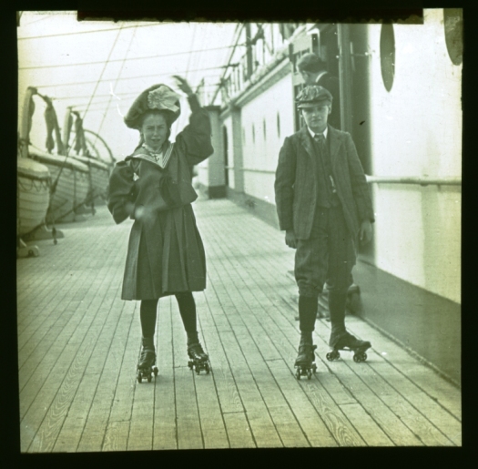 A view of the deck on-board the Mauretania, with a young boy and girl skating along the deck.