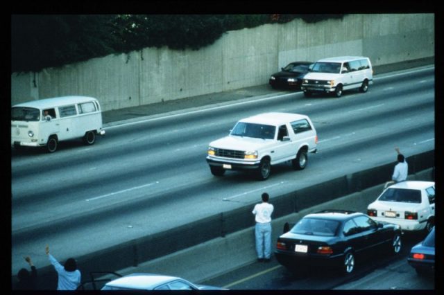 Motorists wave as police cars pursue the white Ford Bronco driven by Al Cowlings, carrying fugitive murder suspect O.J. Simpson, on a 90-minute slow-speed car chase June 17, 1994 on the 405 freeway in Los Angeles, California.  (Photo by Jean-Marc Giboux/Liaison)