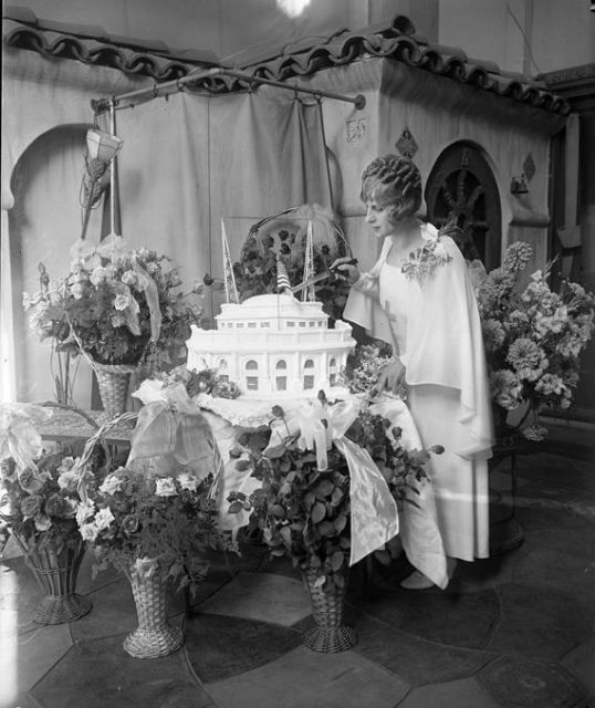 McPherson surrounded by flowers, cutting into Angelus Temple cake, 1929.