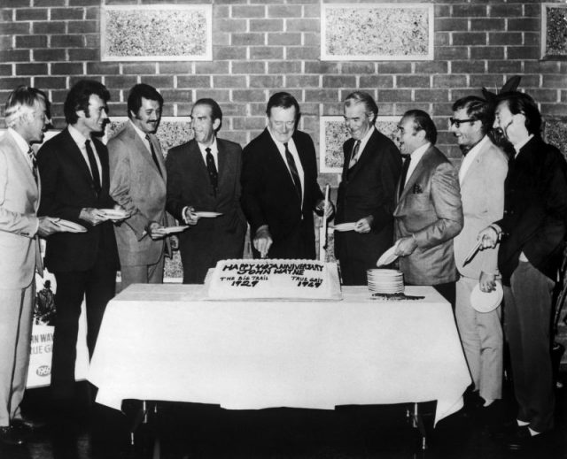 American actor John Wayne cutting the cake of its 40th anniversary of a movie career in Hollywood, California in 1969, with from left to right: Lee Marvin, Clint Eastwood, Rock Hudson, Fred MacMurray, James Stewart, Ernest Borgnine, Michael Caine and Laurence Harvey. Photo by Keystone-France/Gamma-Keystone via Getty Images
