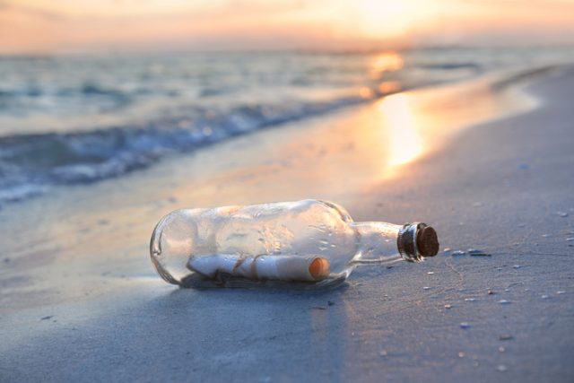 Message in a bottle resting on shore during sunset