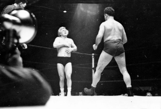 A wrestler strides toward Gorgeous George who stands near a corner of the ring with his hands on his chest where he had received a blow in the previous maneuver in the wrestling match. Photography by S. Kubrick.