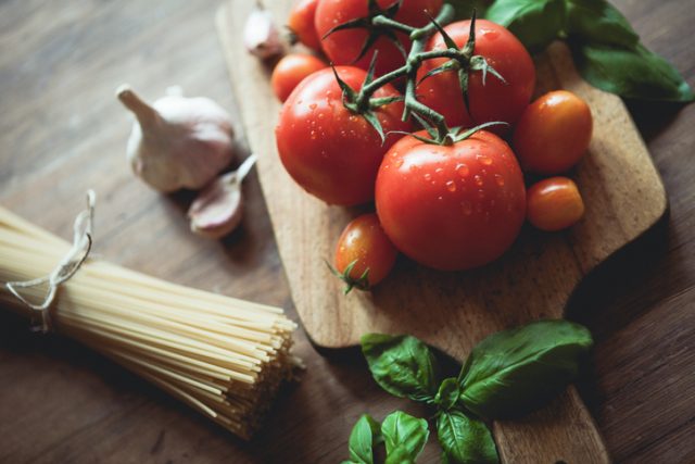 Spaghetti, garlic, basil and tomatoes on a cutting board.