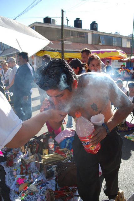 A man blowing smoke onto a miniature image of Santa Muerte. Photo by Thelmadatter CC BY-SA 3.0