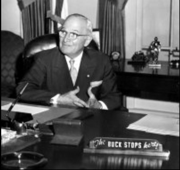 At the recreation of the Truman Oval Office at the Truman Library in 1959, the former President Truman poses by his old desk which has the famous “The Buck Stops Here” sign