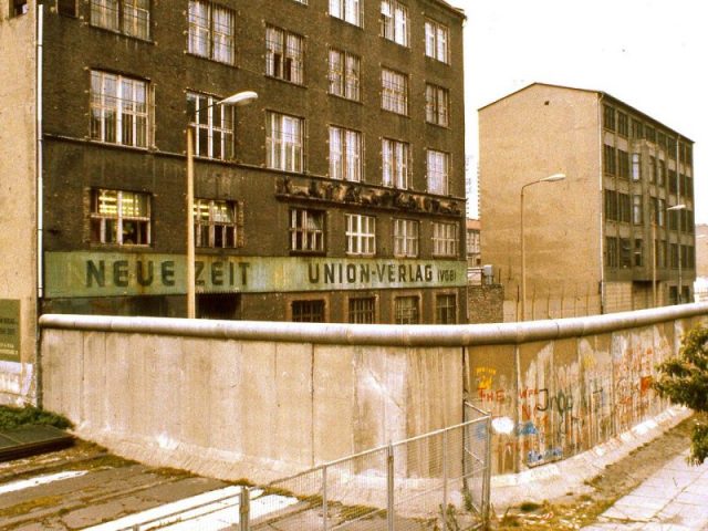 1984 – the top of the Berlin Wall was lined with a smooth pipe, intended to make it more difficult to scale. The areas just outside the wall, including the sidewalk, are de jure Eastern Bloc territory. Photo by GeorgeLouis CC BY-SA 3.0