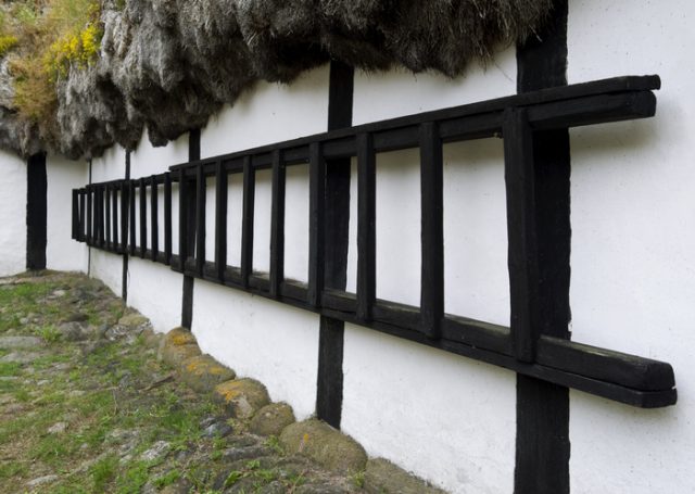 Long wooden ladder hanging on the wall of an old half-timbered farmhouse thatched with a seaweed roof on the Kattegat island of Laesoe