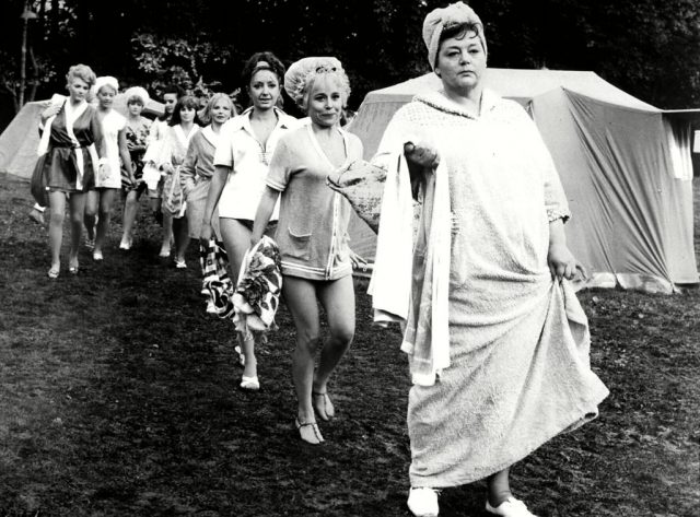 Women from Carry on Camping walking in a line with their robes and bath towels