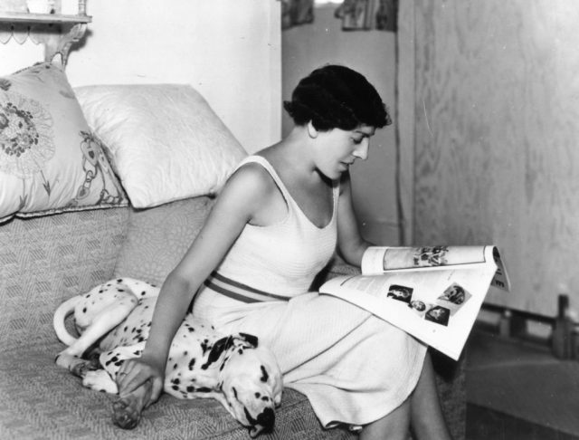Dodie Smith, author of The One Hundred and One Dalmatians, sitting next to a Dalmatian while reading a newspaper