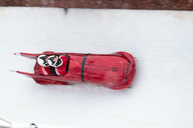 Two Olympic athletes riding in a red bobsleigh