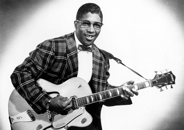 Bo Diddley dressed in a suit and playing a guitar
