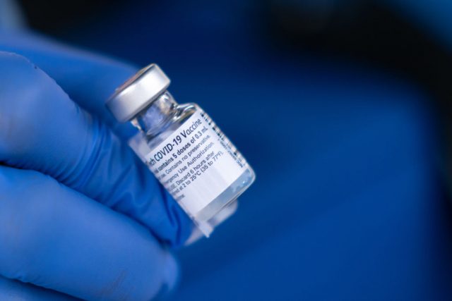 Gloved hands holding a vial of the coronavirus vaccine