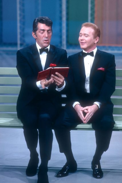 Dean martin and red buttons reading a book while sitting on a bench
