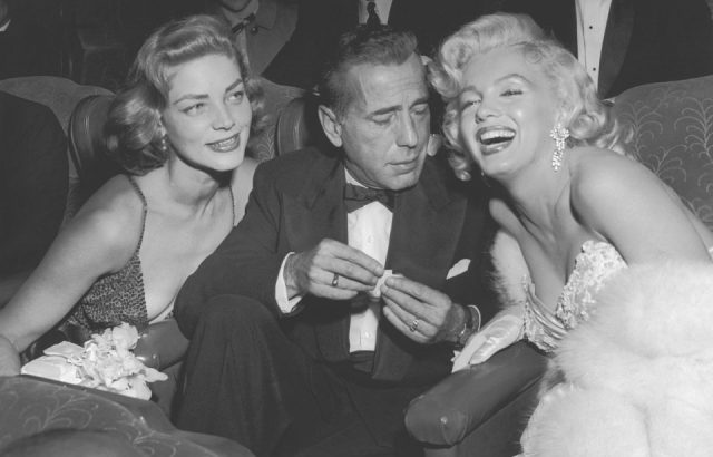 Married American actors Lauren Bacall (L) and Humphrey Bogart (1899 - 1957) pose with American actor Marilyn Monroe (1926 - 1962) at the premiere of director Jean Negulesco's film, 'How to Marry a Millionaire'.