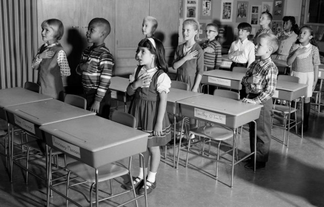 1960s BOYS AND GIRLS SAYING PLEDGE OF ALLEGIANCE IN CLASSROOM