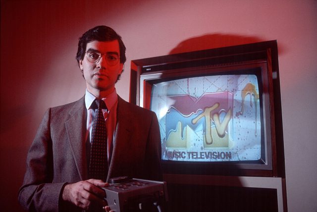 Mtv founder bob pittman standing in front of a tv with the channel's logo