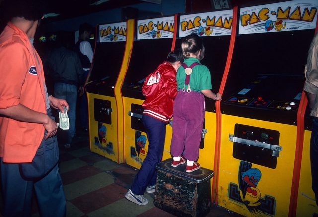 Two children playing Pac-Man at an arcade